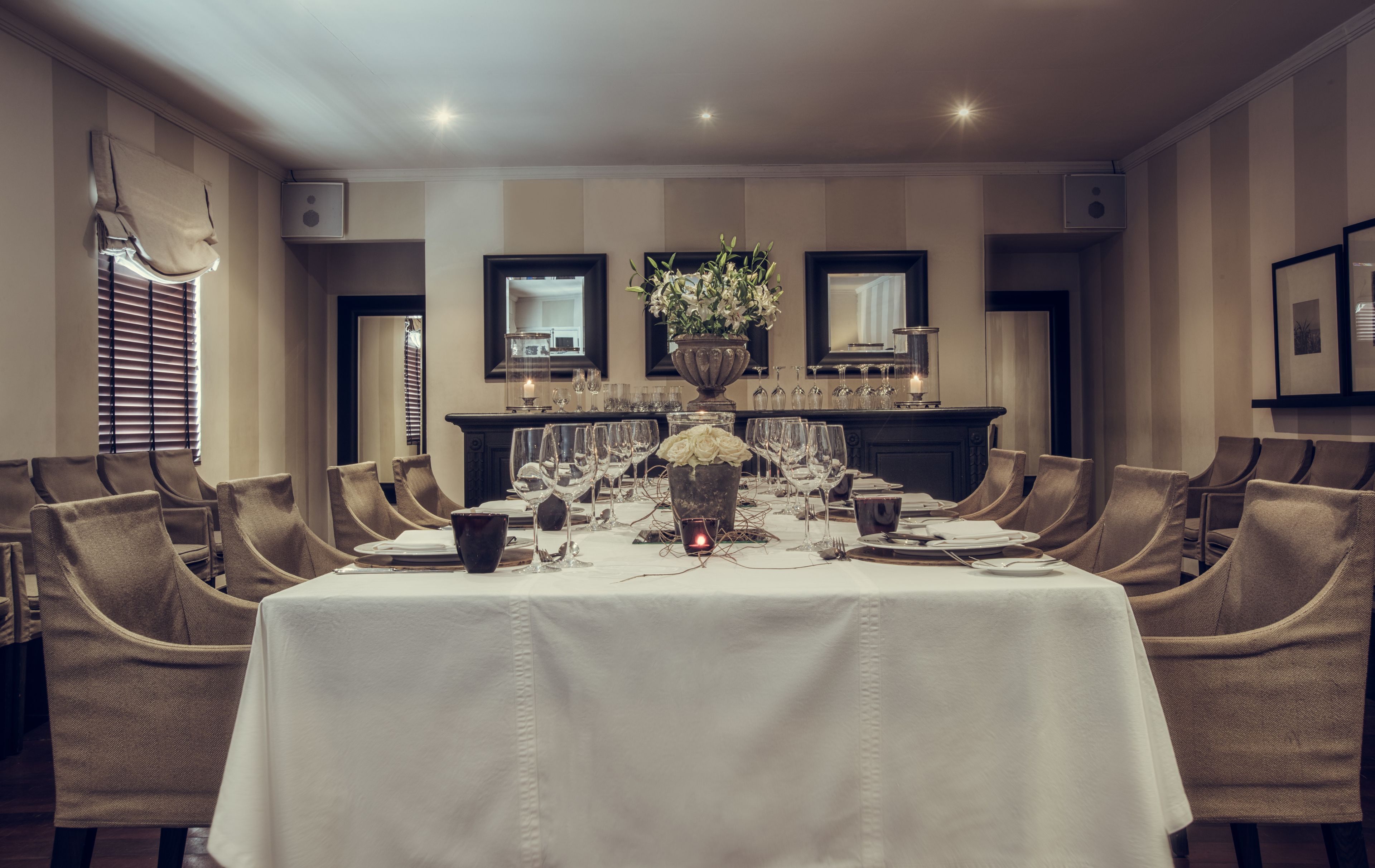 A formal dining room with a long table set for a meal, surrounded by upholstered chairs.