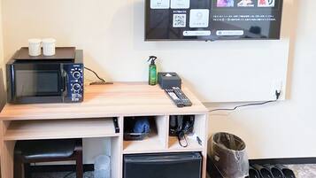 A compact kitchenette with a microwave, two small containers, a remote control, and a trash bin.