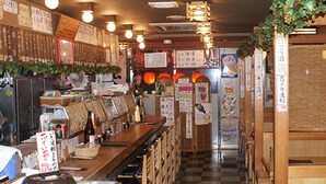Interior de un restaurante con una barra larga, sillas de madera y varios carteles y menús en las paredes.
