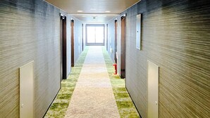 Un pasillo largo y estrecho con alfombra estampada, iluminación empotrada y un extintor en la pared.