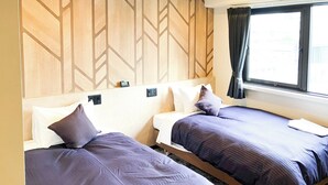 Una habitación de hotel con dos camas, cada una con cabecero, y una ventana con cortinas.