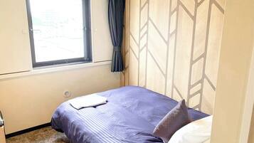 Ein kleines, ordentlich eingerichtetes Schlafzimmer mit einem Einzelbett, einem Fenster mit Vorhängen und einer Wand mit Muster.