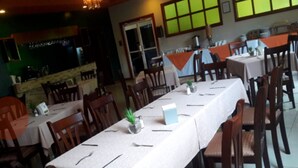 A restaurant with long tables, wooden chairs, and a bar area.