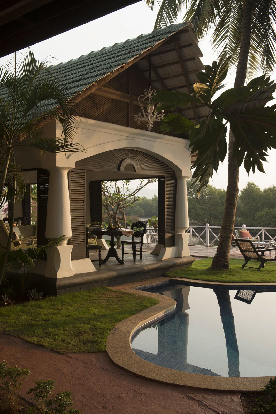 A covered outdoor seating area with a pool, palm trees, and a view of the landscape.