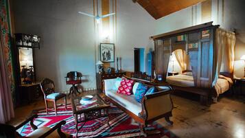 Una habitación tradicional con sofá, una silla de madera, una mesa de centro de vidrio, alfombra estampada y cama con dosel.