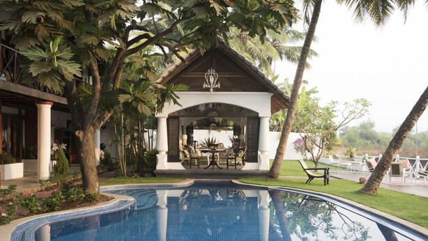 A pool with a covered seating area, surrounded by palm trees and a well-maintained lawn. - Casa Britona (Alto de Porvorim)