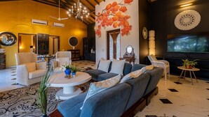 A spacious living room with a large sofa, a coffee table, and a chandelier. There are multiple chairs and a TV mounted on the wall. - Casa Britona (Alto de Porvorim)