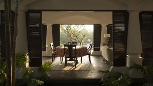An outdoor dining area with a round table and chairs, surrounded by bamboo plants and a view of greenery. - Casa Britona (Alto de Porvorim)