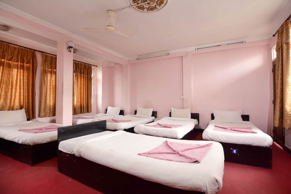 Ein Hotelzimmer mit vier Einzelbetten, einem roten Teppich und einem Deckenventilator.