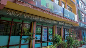 A multi-story hotel with balconies, a sign for "Silver Mountain Adventure Ltd. Hotel," and potted plants along the sidewalk. - Hotel Silver Home - Hostel (Kathmandu)