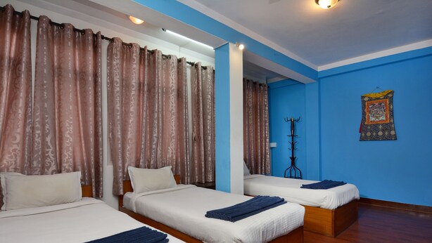 A hotel room with two beds, blue walls, and curtains. - Hotel Silver Home - Hostel (Kathmandu)