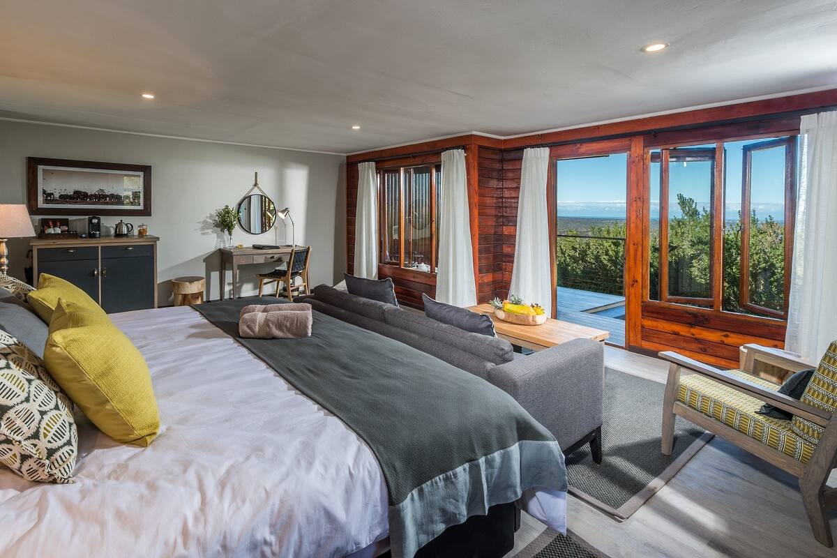 A spacious bedroom with a large bed, a sofa, a desk, and a view of the outdoors.