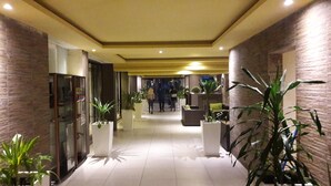 A modern hotel lobby with a tiled floor, potted plants, and a seating area. - Retaj Moroni Hotel (Moroni)