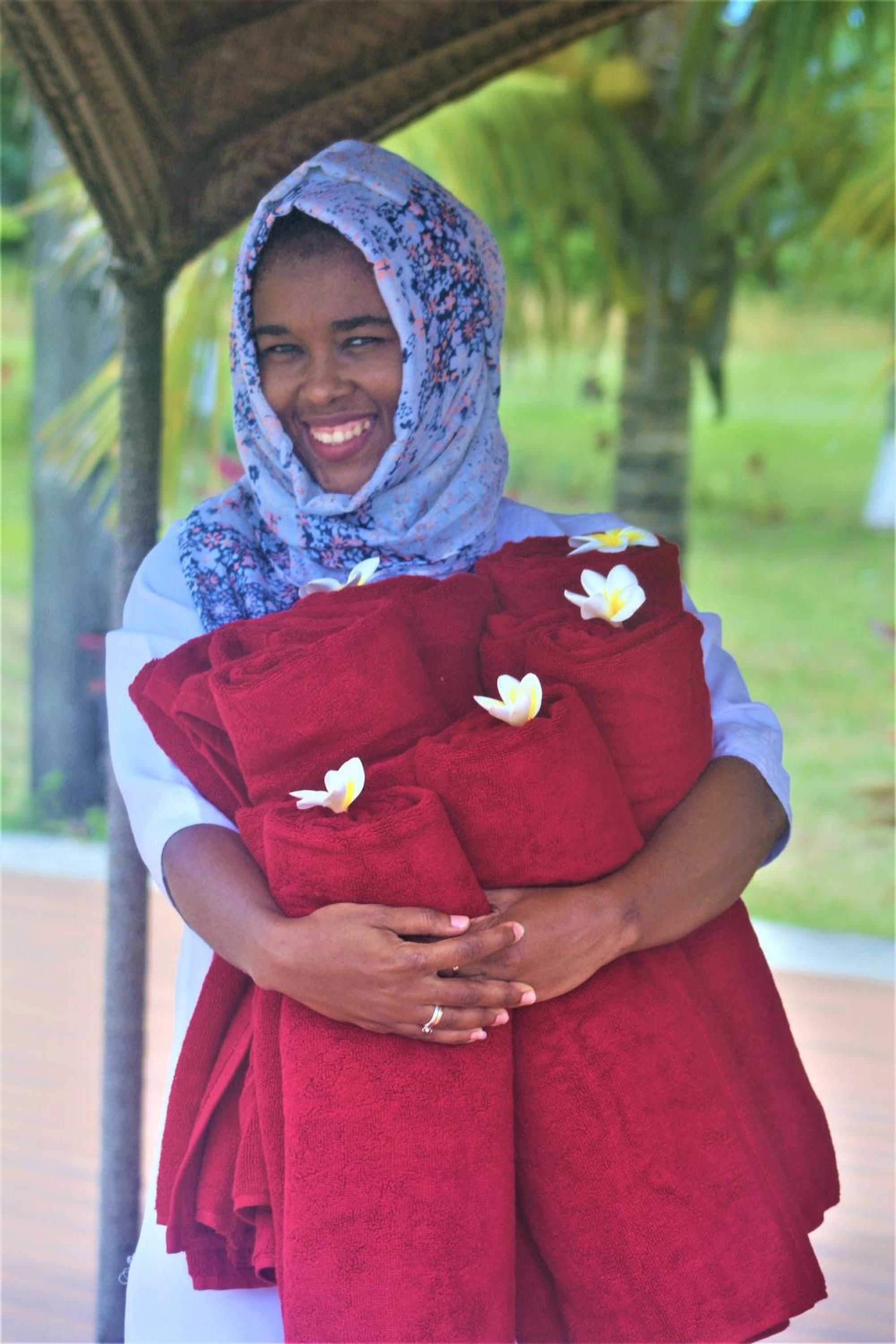 A person holding a red blanket with white flowers, standing under a shelter with palm trees in the background.