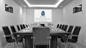 A conference room with a long table, chairs, and a logo on the wall. - Retaj Moroni Hotel (Moroni)