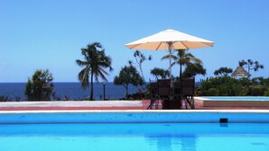 A pool with a clear view of the ocean, surrounded by palm trees and a beach. - Retaj Moroni Hotel (Moroni)