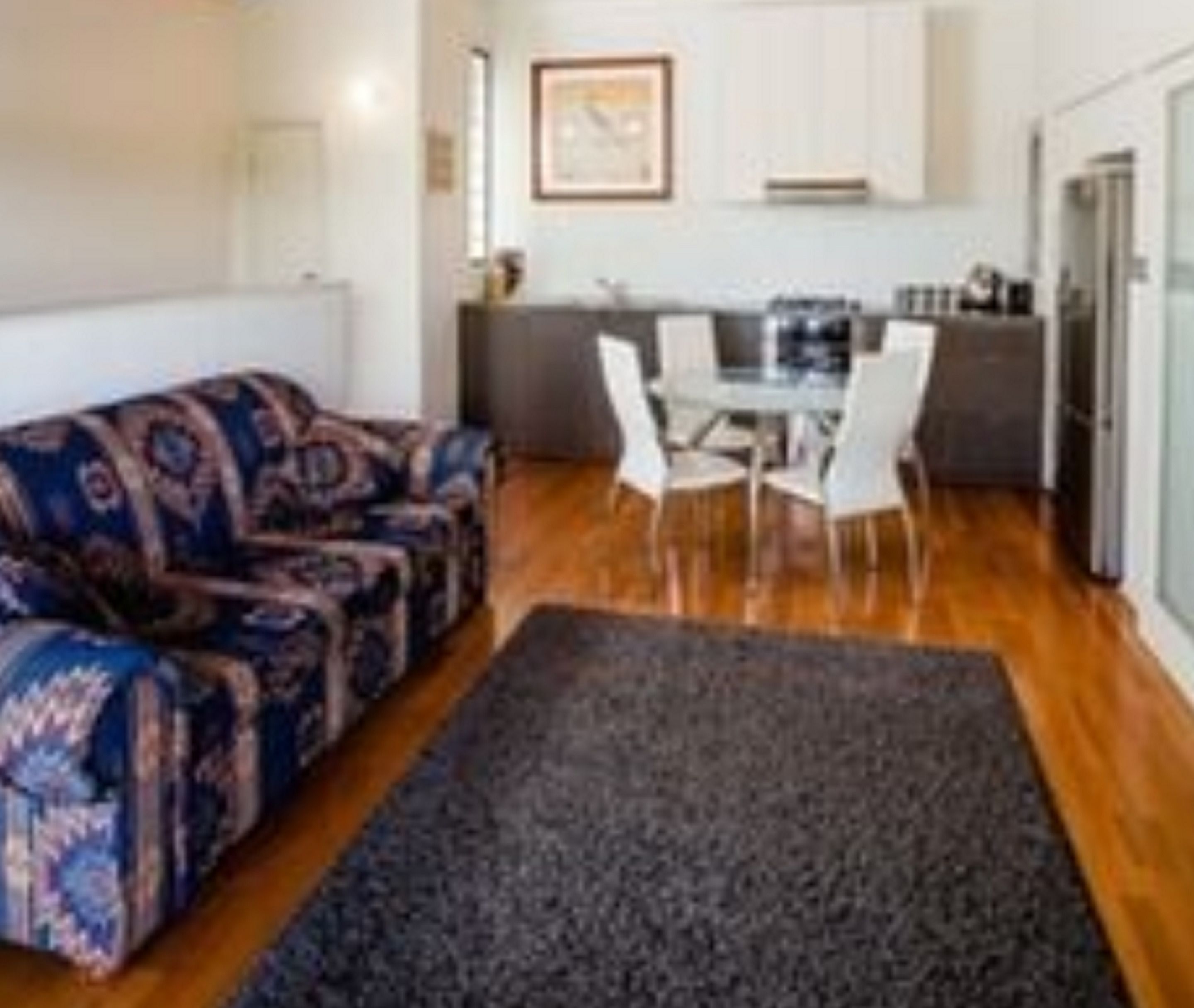 Una sala moderna con un sofá estampado, una mesa de comedor con sillas y una cocina al fondo.