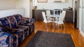 Una sala moderna con un sofá estampado, una mesa de comedor con sillas y una cocina al fondo.