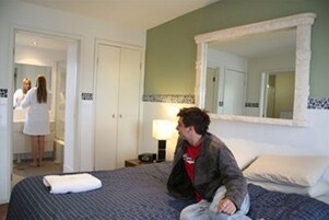 Quarto de hotel com cama, mesa de cabeceira, espelho e porta para o banheiro.