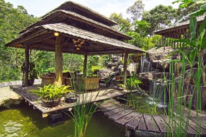 A rustic wooden structure with a thatched roof, surrounded by lush greenery and a small waterfall. - Fig Tree Hill Resort (George Town)