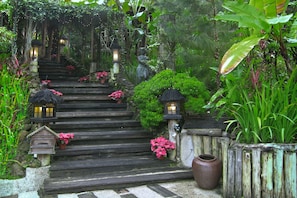 A wooden staircase with lanterns, potted plants, and a rustic fence in a lush garden setting. - Fig Tree Hill Resort (George Town)