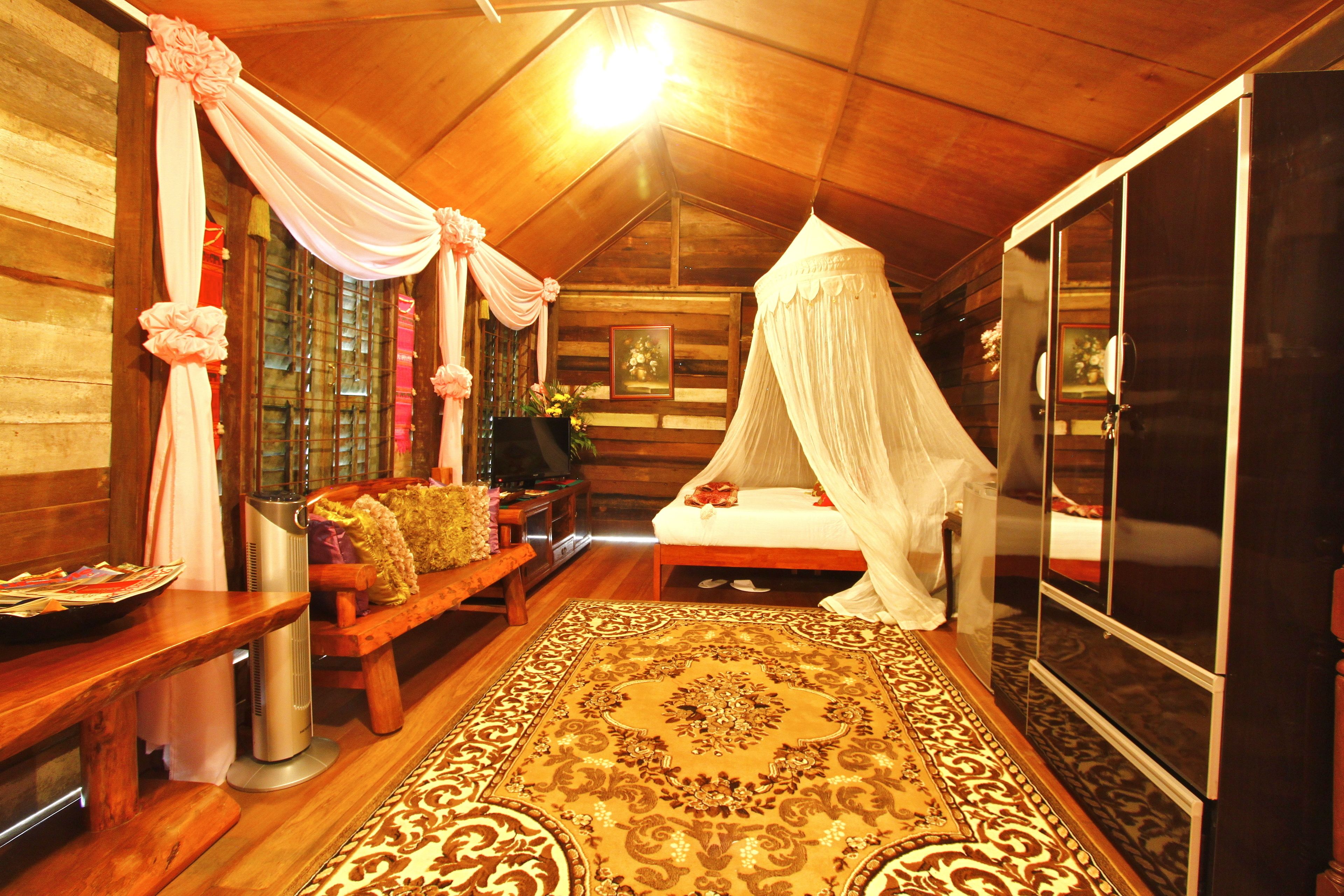 Une pièce chaleureuse avec un plafond en bois, un lit à baldaquin, un banc, une télévision et un grand tapis.