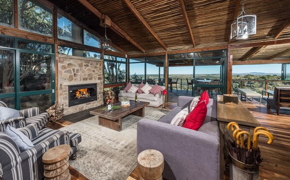 A spacious living area with a stone fireplace, comfortable seating, and large windows offering scenic views.