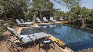 Una piscina al aire libre, sombrillas, sillones reclinables de piscina