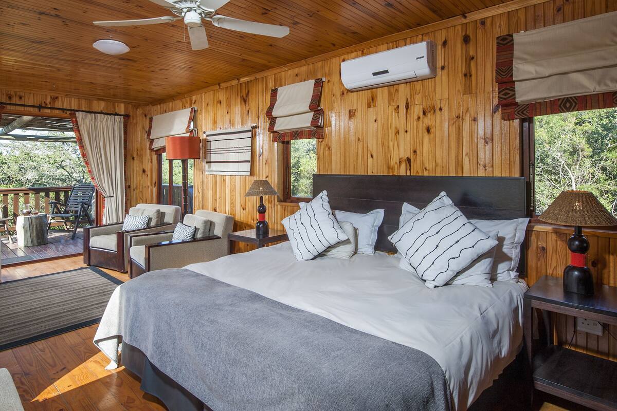 Une chambre dans une cabane en bois, avec un grand lit, deux chaises, un bureau et un téléviseur.