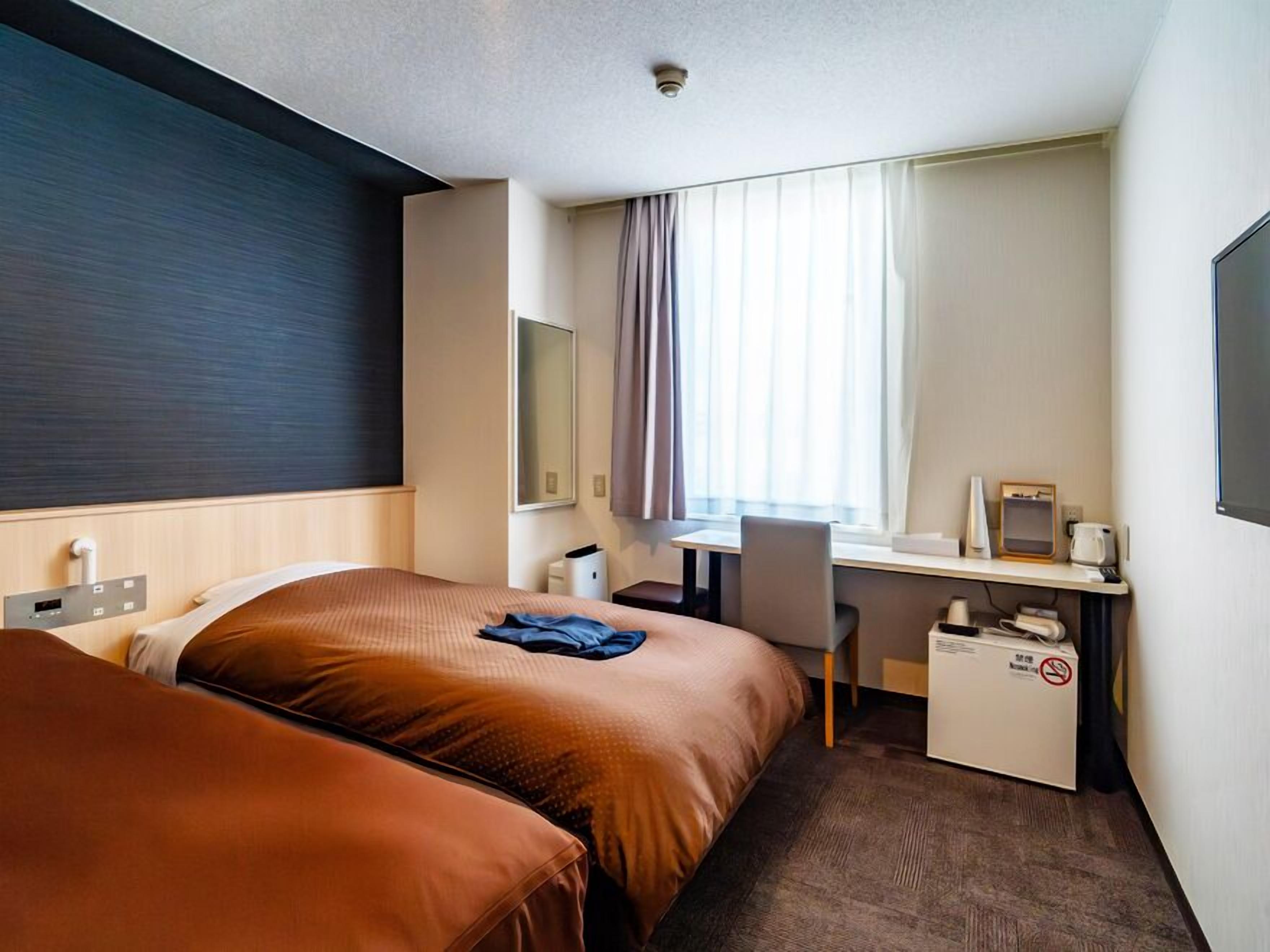 Hotelkamer met twee bedden, een bureau, een stoel, een televisie en een raam met gordijnen.