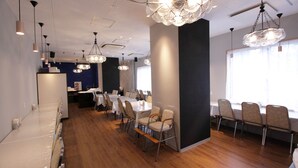 Un espace repas moderne avec un plancher en bois, des tables et des chaises blanches, ainsi que des lustres en cristal décoratifs.