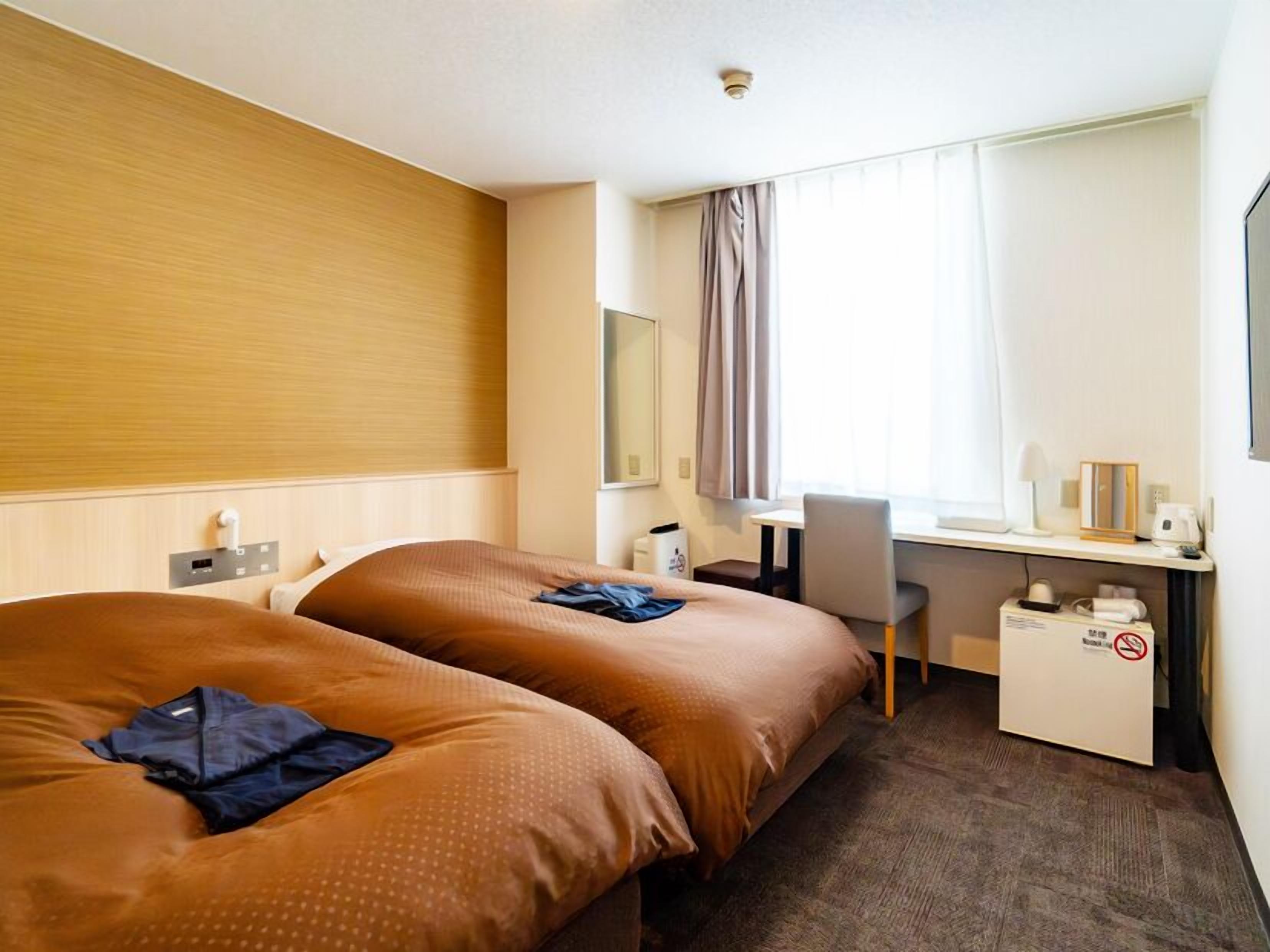 Hotelkamer met twee bedden, een bureau, een stoel, een raam met gordijnen en een klein tafeltje met een koffiezetapparaat.