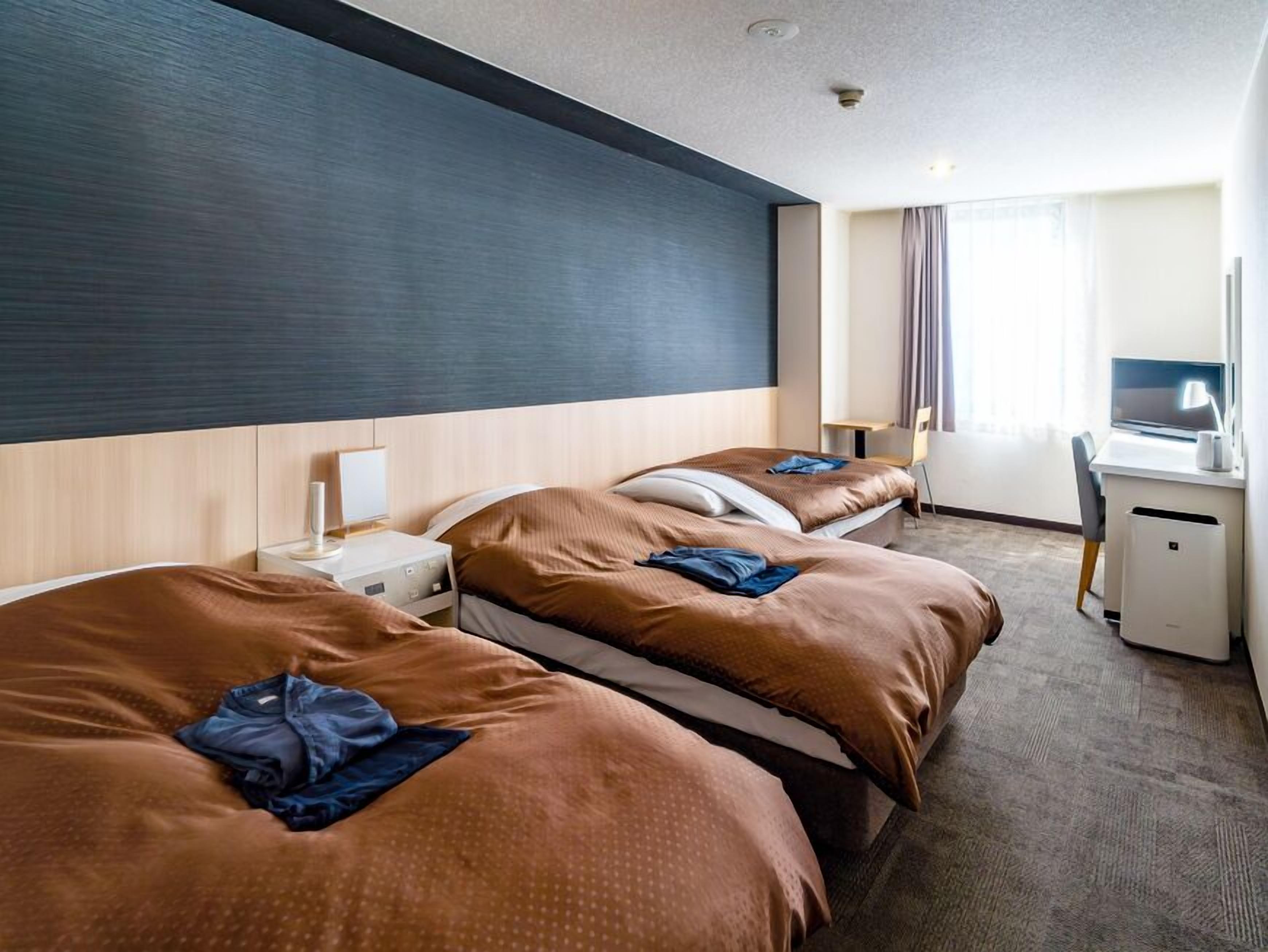 Een hotelkamer met twee bedden, een bureau, een stoel, een lamp en een raam met gordijnen.