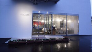 Un bâtiment moderne doté de grandes fenêtres en verre, d’une entrée abritée et de plantes en pot devant la façade.