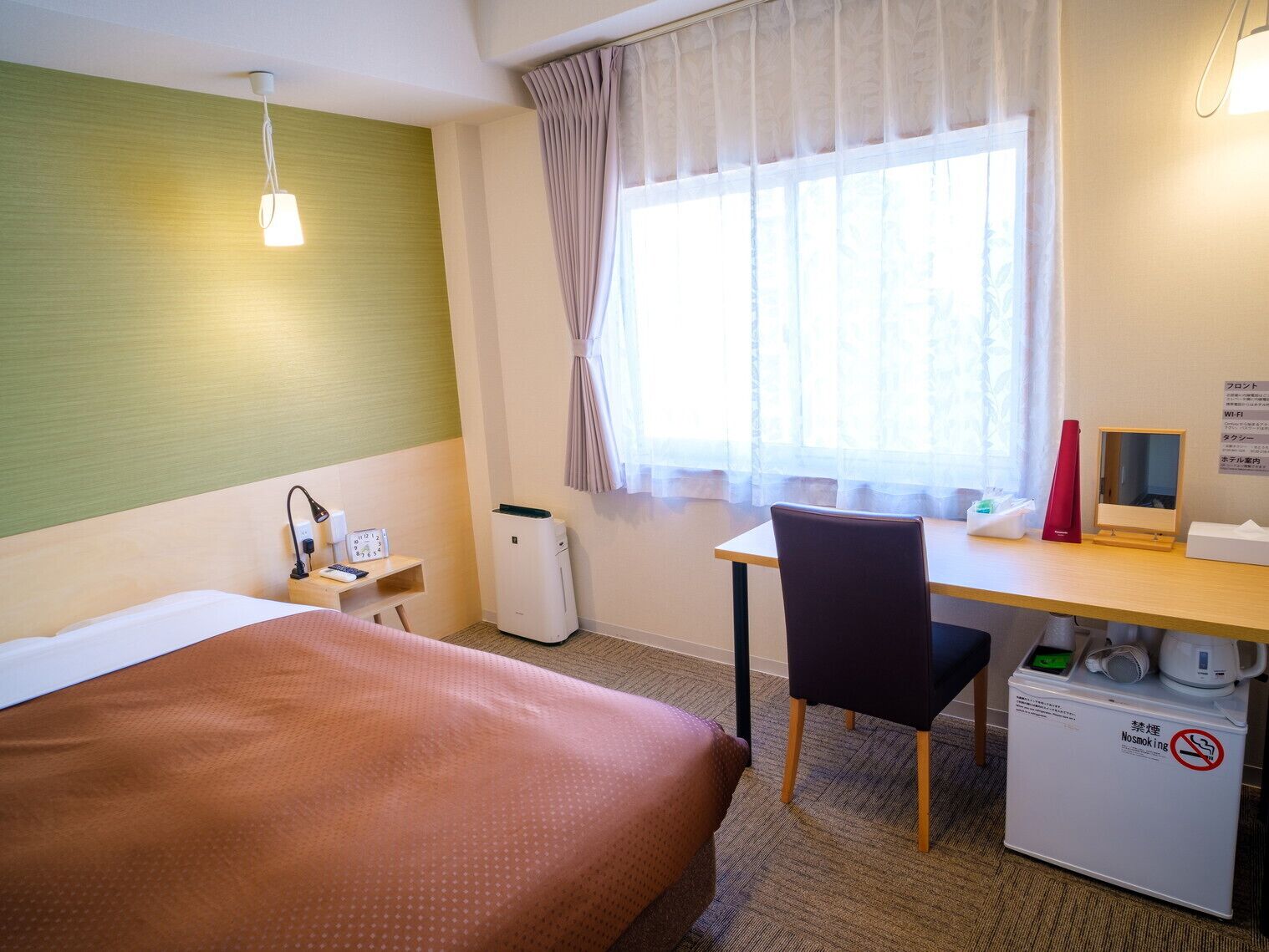 Een hotelkamer met een bed, bureau, stoel en een compact luchtreiniger.