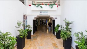A hotel corridor with a double-height balcony decorated with red flowers, potted plants on either side, and a sign for the hotel.
