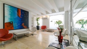 A modern office space with a large abstract painting, white furniture, and a view through large windows.