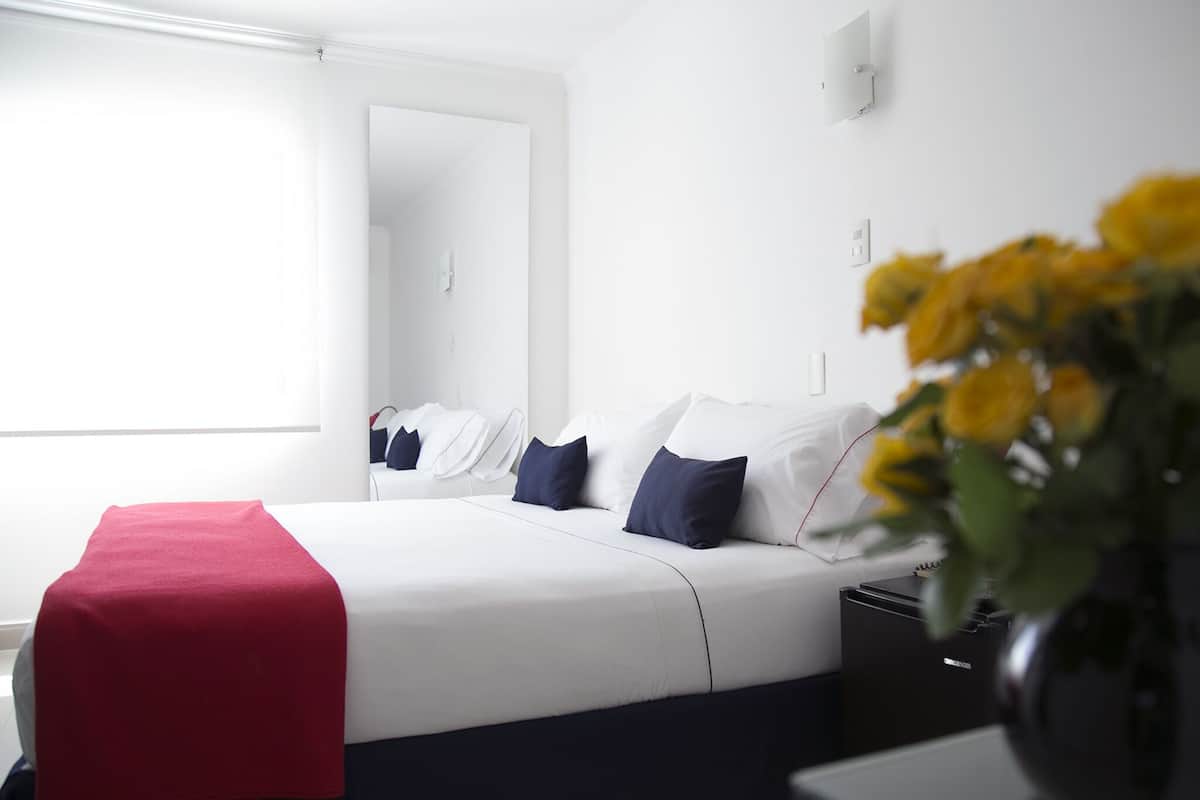 Ein modernes Hotelzimmer mit einem großen Bett, einer roten Tagesdecke und einer Vase mit gelben Blumen.