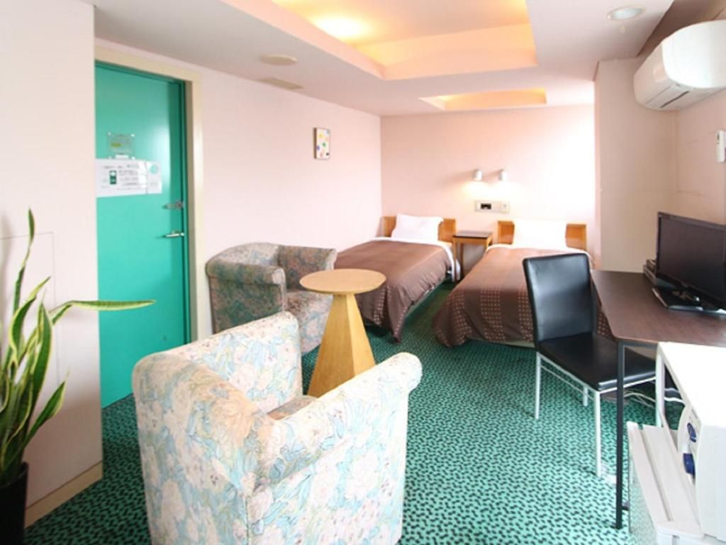A hotel room with a bed, two bedside tables, a desk with a chair, a television, and a green door.