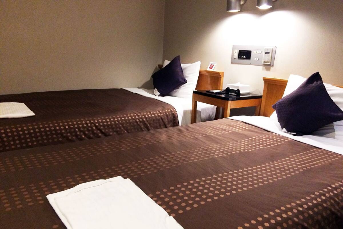 Ett hotellrum med två sängar, ett nattduksbord i trä, en telefon och en väggmonterad kontrollpanel.