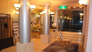 A lobby with a reception desk, a flower arrangement, and a staircase leading to an elevator. - Hotel Live Max Yumoto (Iwaki)