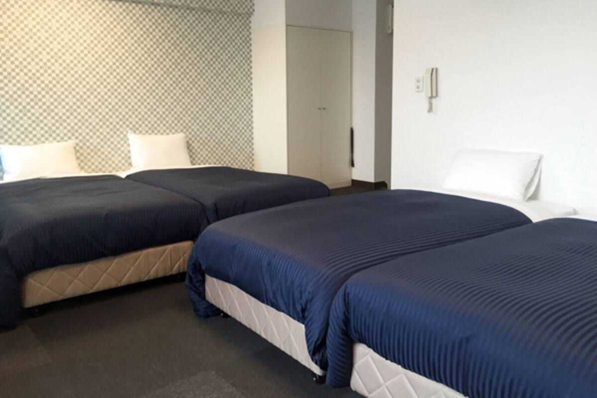 A hotel room with two beds, a patterned headboard, and a door leading to another room.