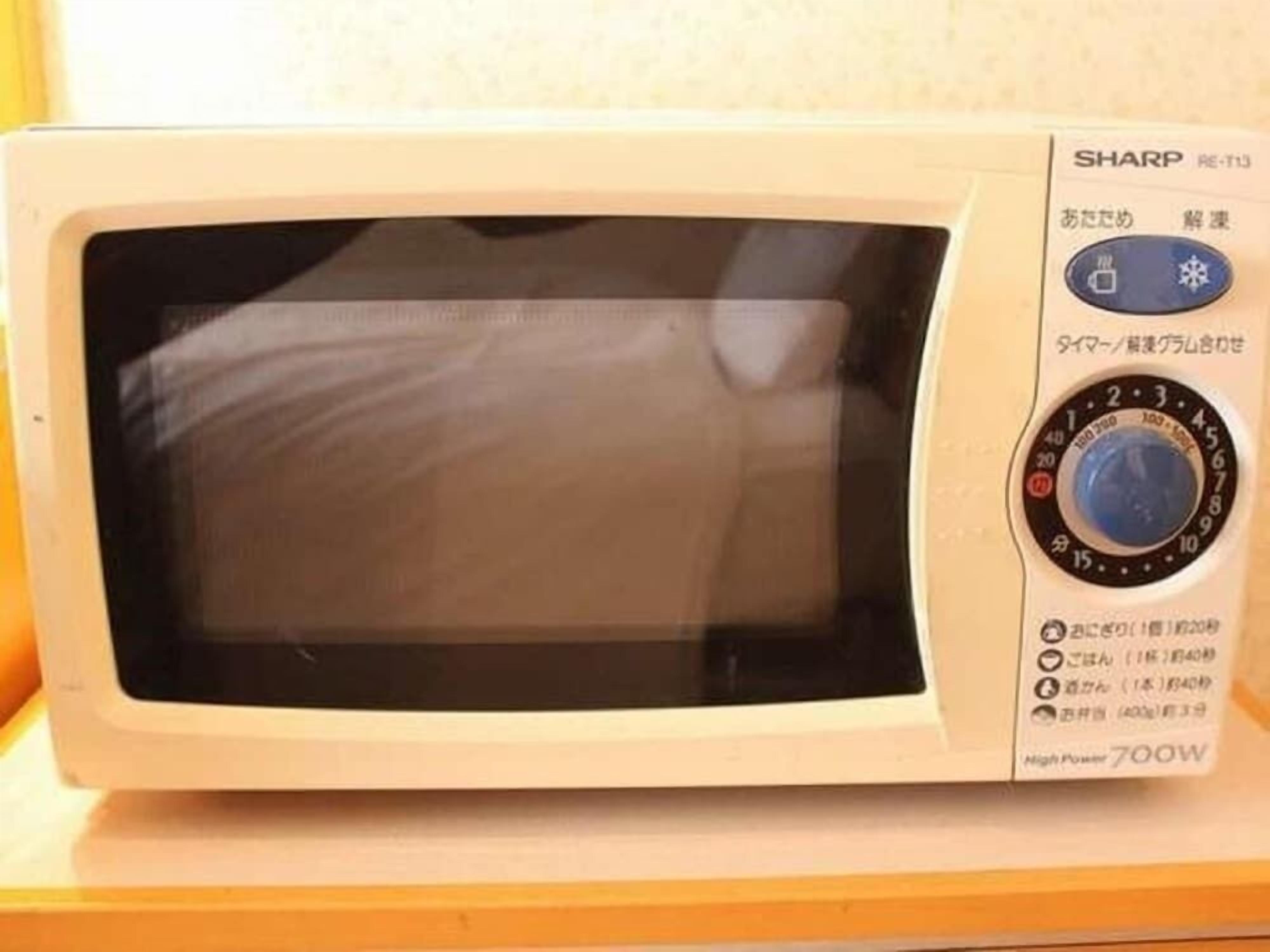 Um micro-ondas com painel de controle, tela de exibição e etiqueta indicando 'SHARP RE-T13' e 'Alta Potência 700W'.
