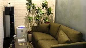 A small living area with a sofa, a coffee table, a water dispenser, and a potted plant. - Hotel Livemax Budget Fuchu (Fuchu)