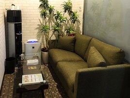 Una pequeña sala de estar con un sofá, una mesita de centro, un dispensador de agua y una planta en maceta.