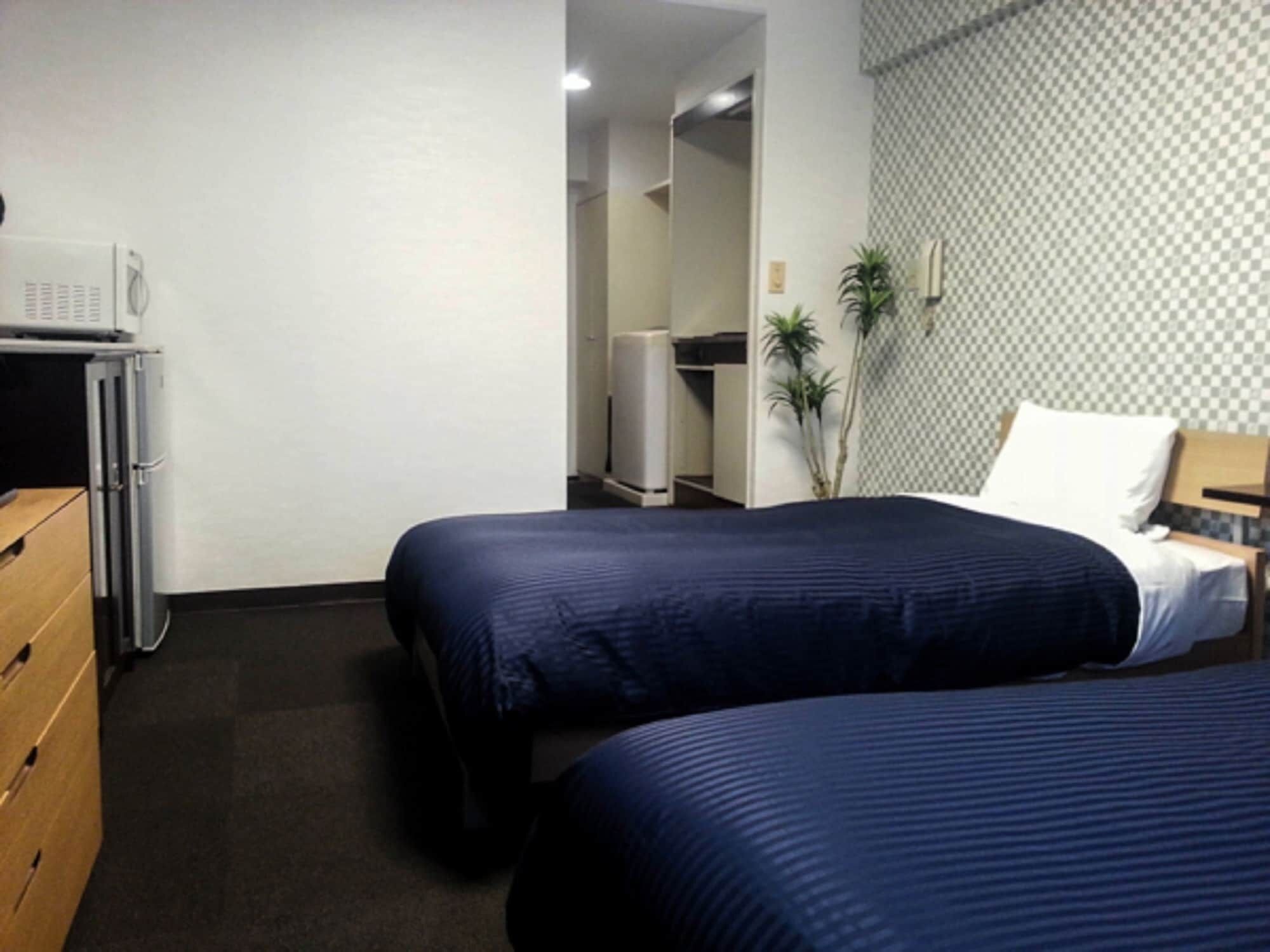A hotel room with two beds, a desk, a chair, a microwave, a refrigerator, and a wardrobe.
