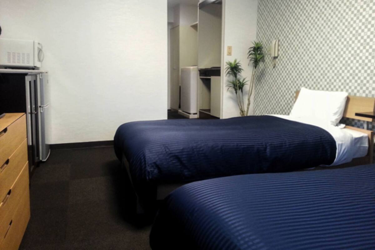 A hotel room with two beds, a desk, a chair, a microwave, and a wardrobe.