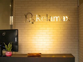 A reception desk with a Dell computer monitor, a potted plant, and a wooden tray. The wall behind features a sign with the word "Relax" illuminated.
