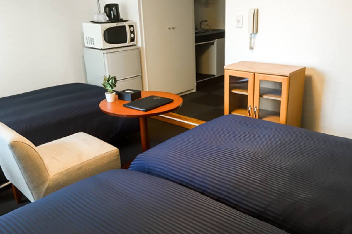 A hotel room with two beds, a small table with a plant, a microwave, and a cabinet.