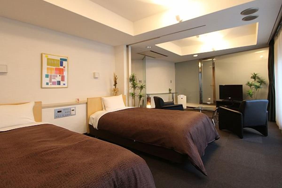 A hotel room with two beds, a desk, a chair, a television, and a mirror.